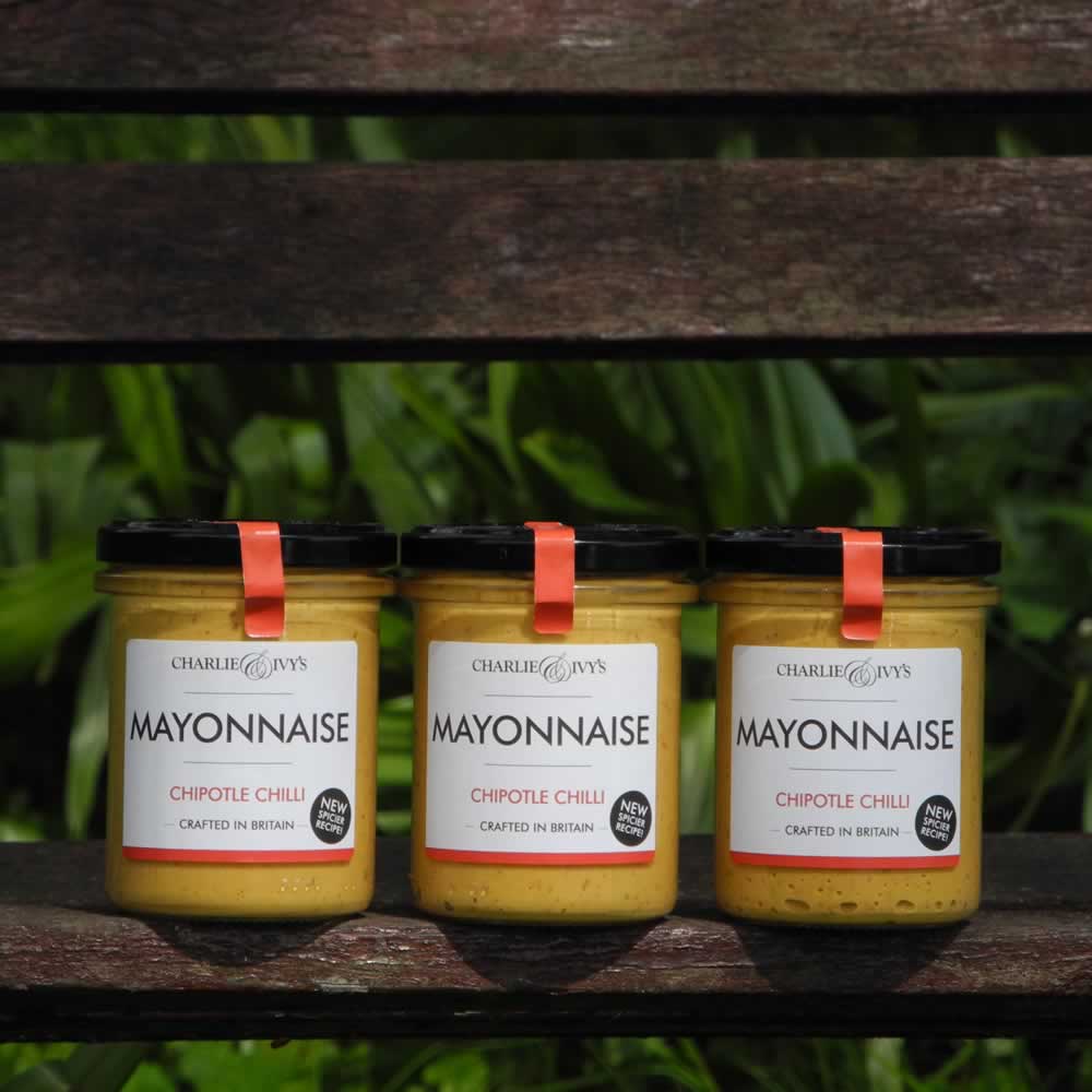 Three jars of Charlie & Ivy's Chipotle Chilli Mayonnaise on wooden bench with plant background