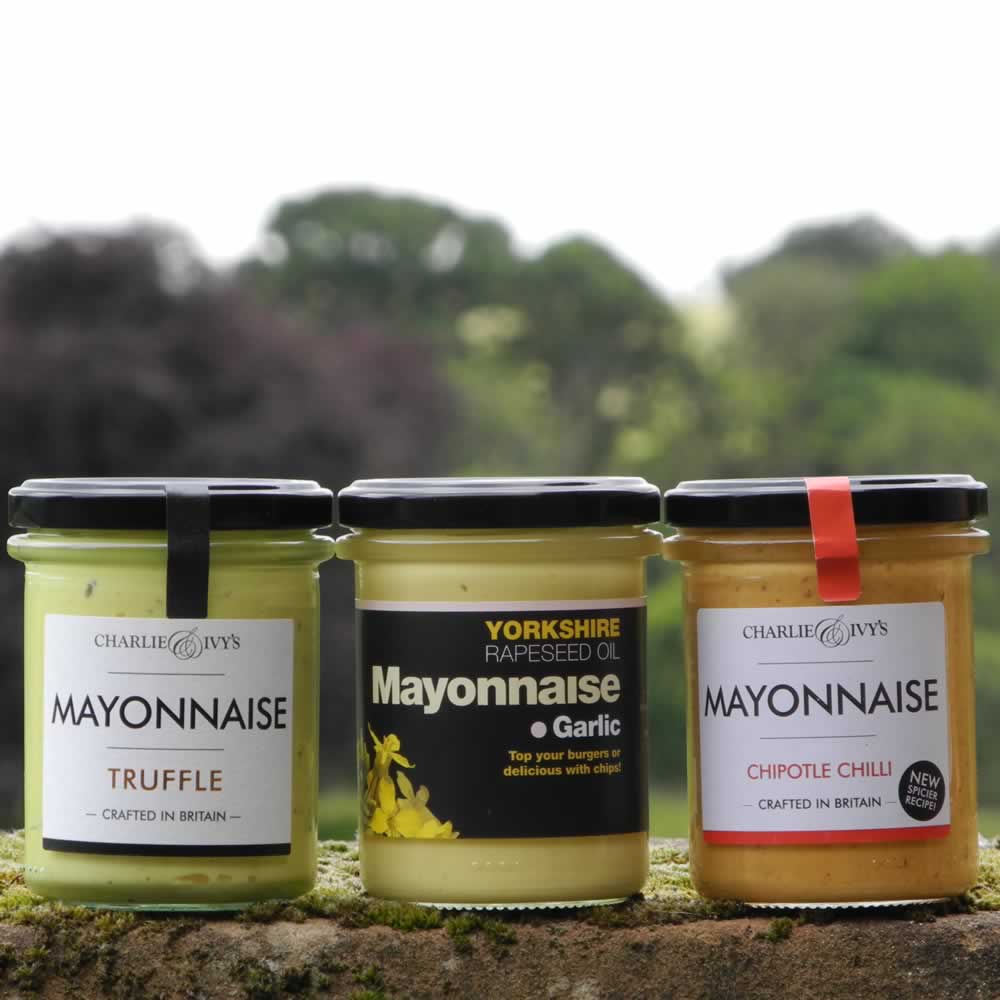 Three jars of mayonnaise, from left to right: Truffle Mayonnaise, Garlic Mayonnaise and Chipotle Chilli Mayonnaise in front of scenic backdrop.