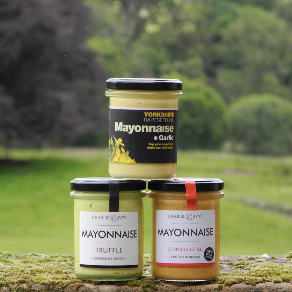 Three jars of mayonnaise stacked on one another, from left to right: Garlic Mayonnaise on top and Chipotle Chilli Mayonnaise and Truffle Mayonnaise at the bottom, in front of scenic backdrop.